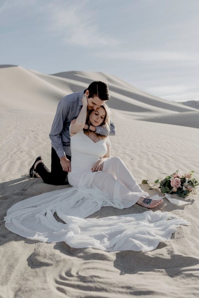 bride and groom sitting on sand dunes in nevada 