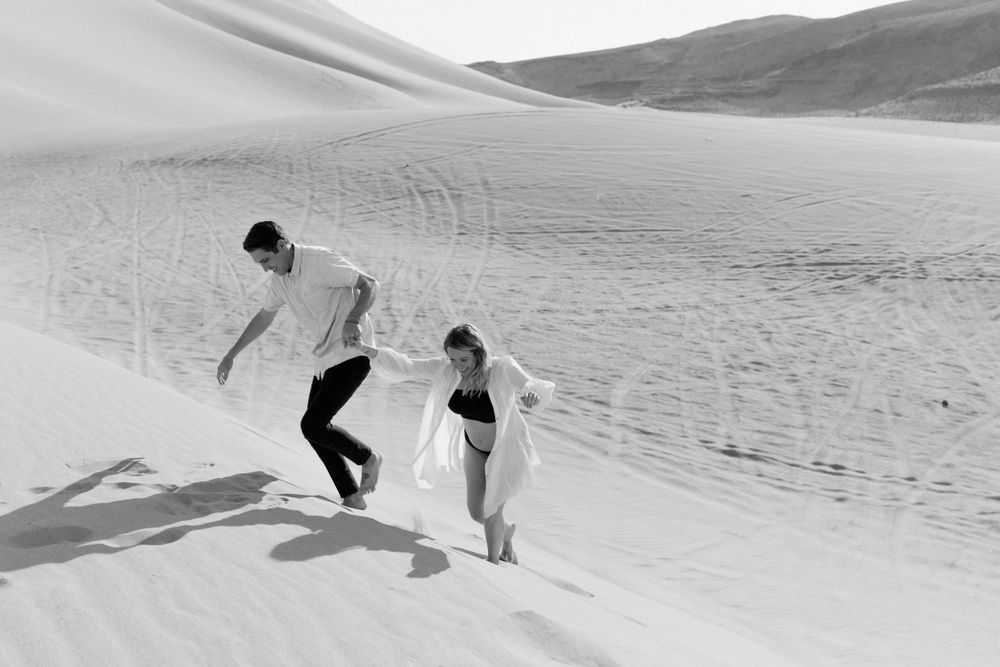 couple running in desert sand dunes during maternity session