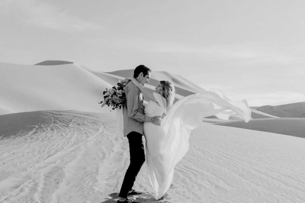 couple holding each other in wedding dress flowing in air in sand dunes nevada by katherine krakowski photography