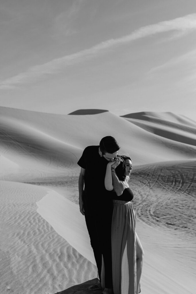 couple kissing hands in desert during maternity session in desert sand dunes by katherine krakowski photography a lake tahoe reno photographer