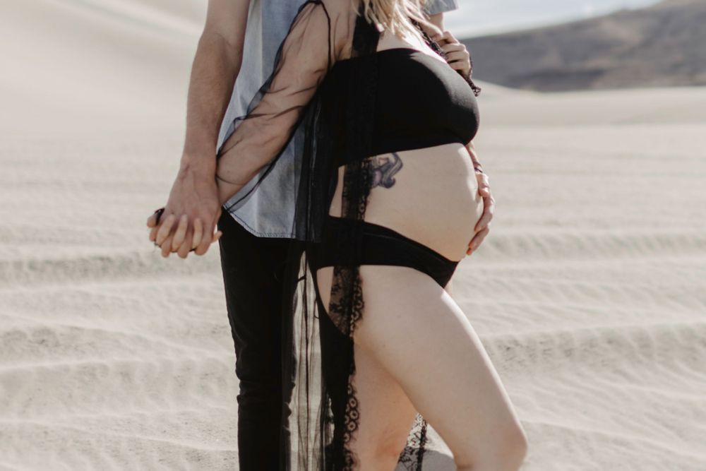close up maternity belly shot and couple is holding hands in desert in sand dunes nevada by katherine krakowski photography a lake tahoe reno photographer