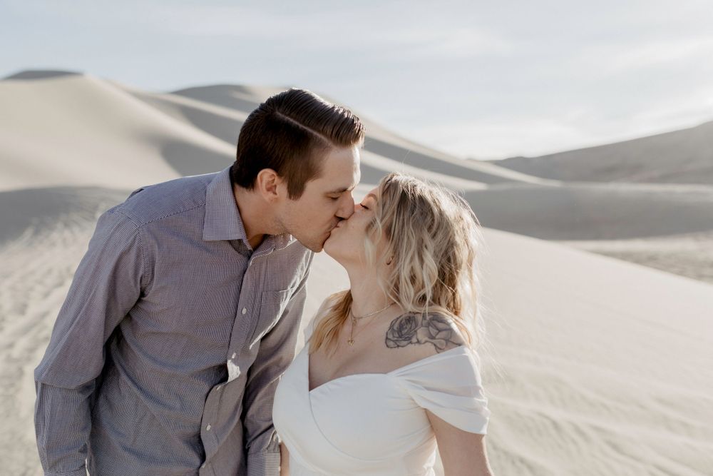 couples close up kissing each other with tattoo showing wearing wedding dress in sand dunes in nevada 