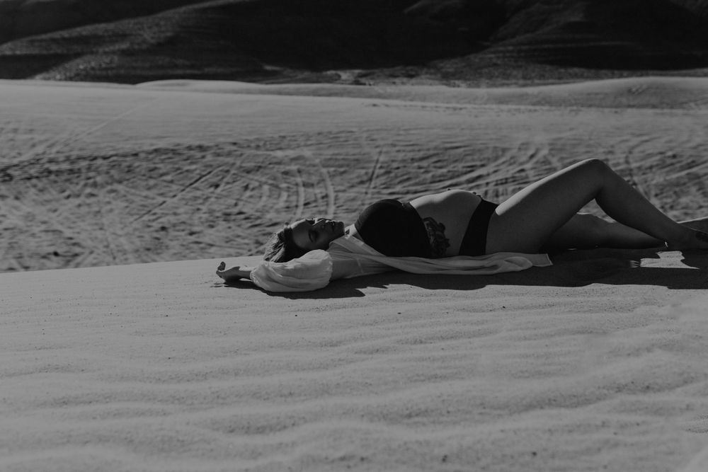 pregnant female laying on sand sand dunes wearing black lingerie and white oversized collar shirt by katherine krakowski photography a lake tahoe reno photographer