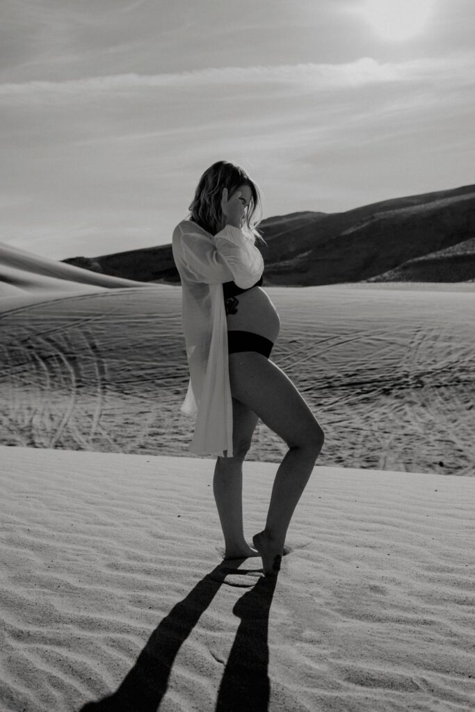 pregnant female in black lingerie and white oversized shirt standing in front of rising sun in the nevada desert sand dunes by katherine krakowski photography a lake tahoe reno photographer