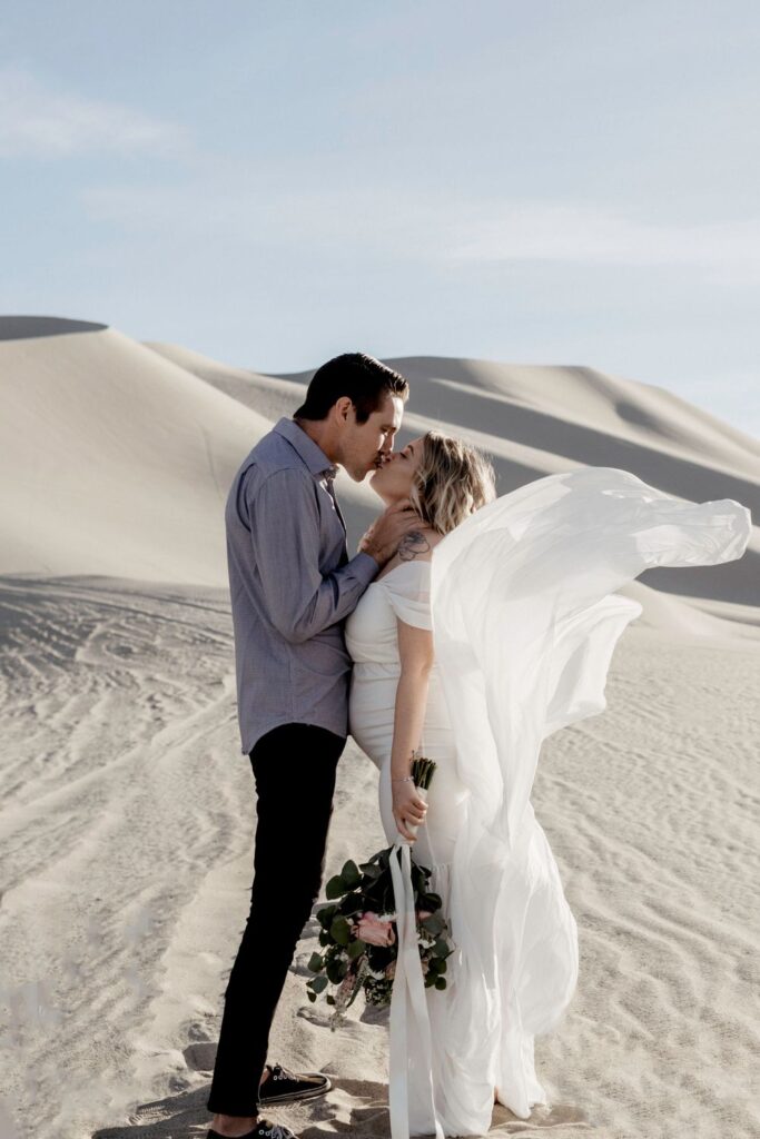 couple kissing in wedding dress flowing in air in sand dunes nevada by katherine krakowski photography