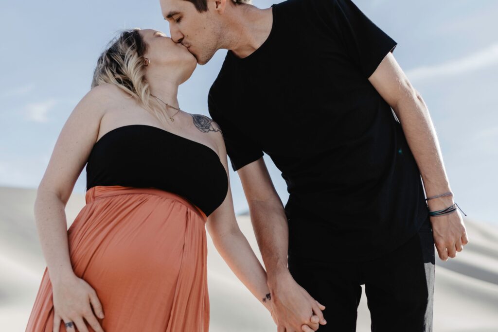 couple holding hands and kissing in desert during maternity session by katherine krakowski photography a lake tahoe reno photographer