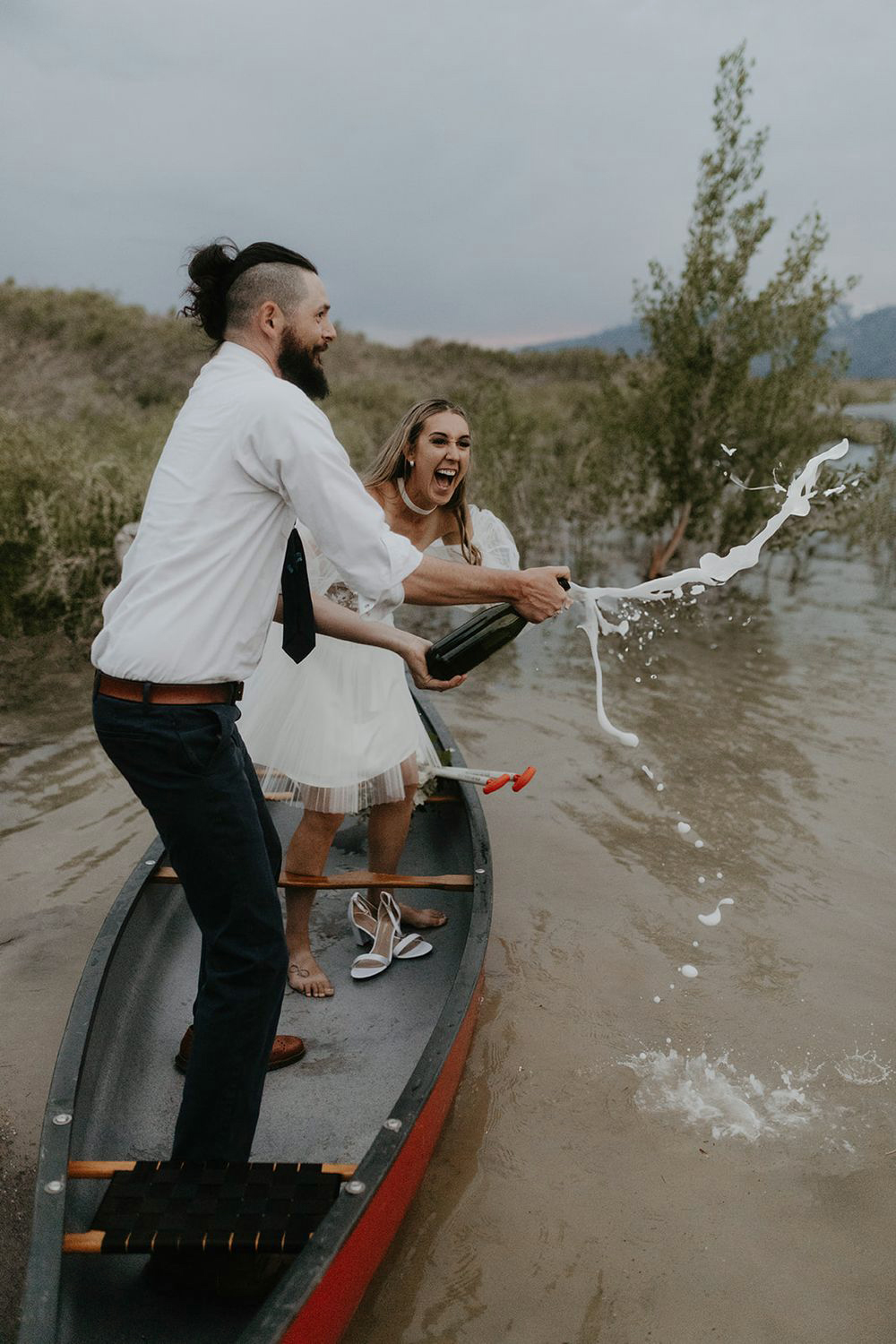 couples popping champagne on canoe in lake with mountains and sunset in background