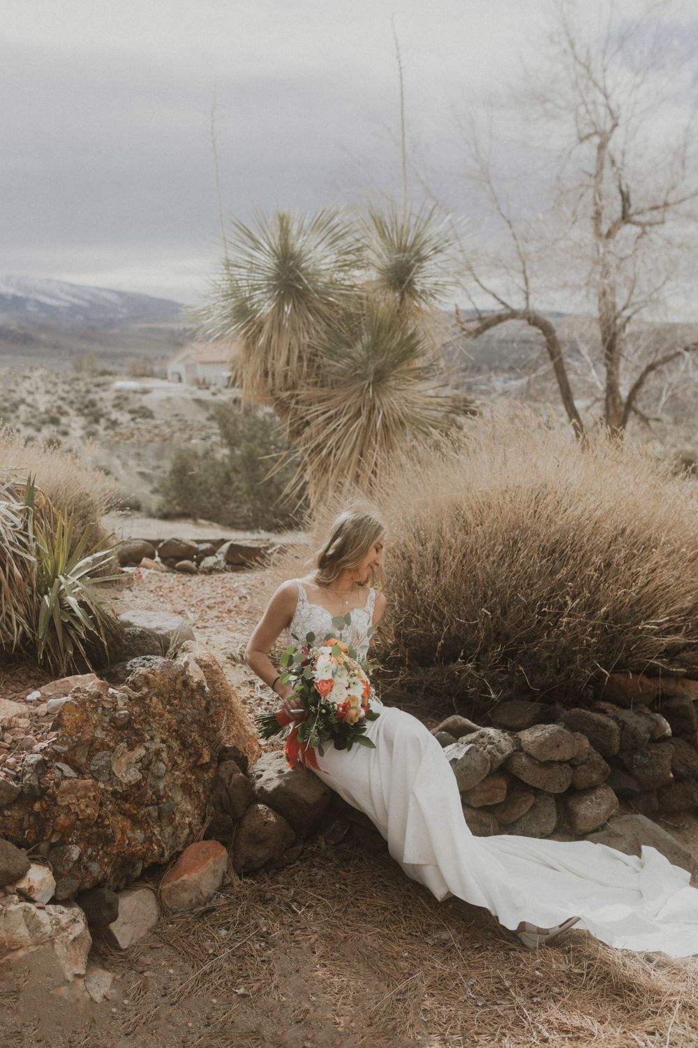 bride sitting in desert wearing wedding gown from aw bridal with vibrant neutral bouquet